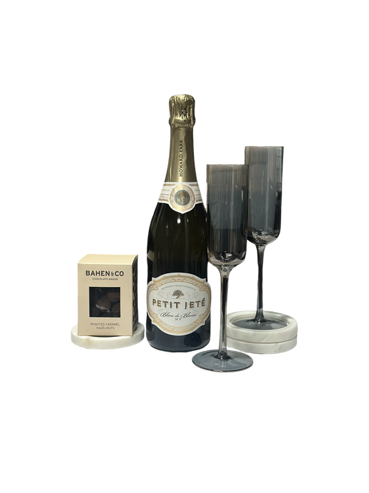 Bottle of Petit Jete champagne with two flutes and a box on a white background