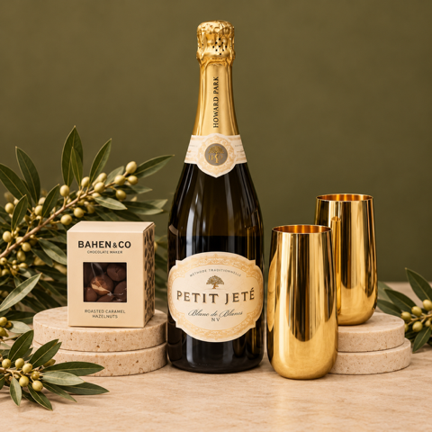 Bottle of Petit Jete champagne with two gold flutes and a box on a beige background