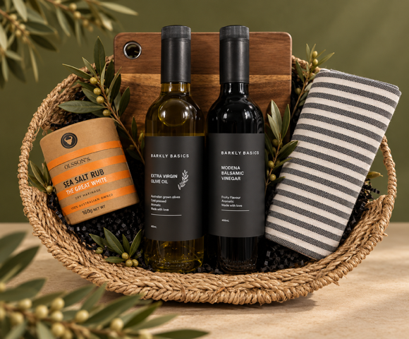 Olive Oil and Balsamic bottles and a jar in a woven basket with a striped towel on a green background
