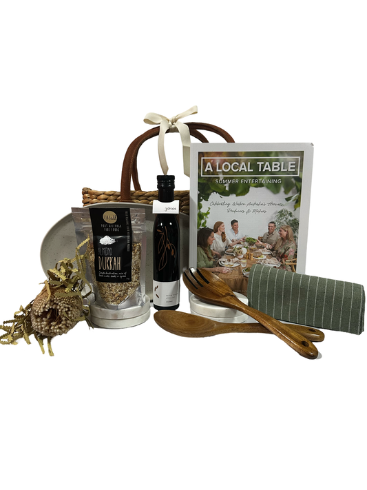 A gift basket containing a cookbook, 'A Local Table,' an ecology serving platter, wooden serving utensils, a striped tea towel, and gourmet products from Western Australia.
