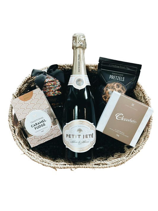 Gift basket with a bottle of Petit Jete champagne, pretzels, and chocolate bars on a white background