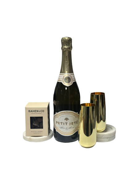 Bottle of Petit Jete champagne with two gold flutes and a box on a white background