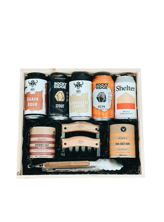 Collection of beer cans, salt rubs and BBQ tools and related items in a box on a white background