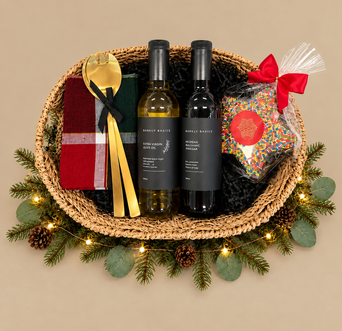 A holiday gift basket set from Simply Brisket, featuring two bottles of wine (one white, one red), a red and green plaid napkin, gold-colored cutlery, and a bag of sprinkles tied with a red bow, all arranged in a woven basket with a pine garland and fairy lights.