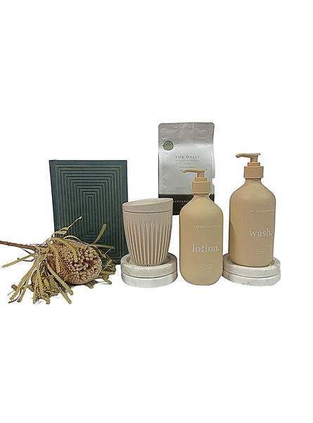 A gift set arrangement including a green bottle of lotion, a green bottle of body wash, a beige suede notebook, a brown huskee cup displayed on a white background.
