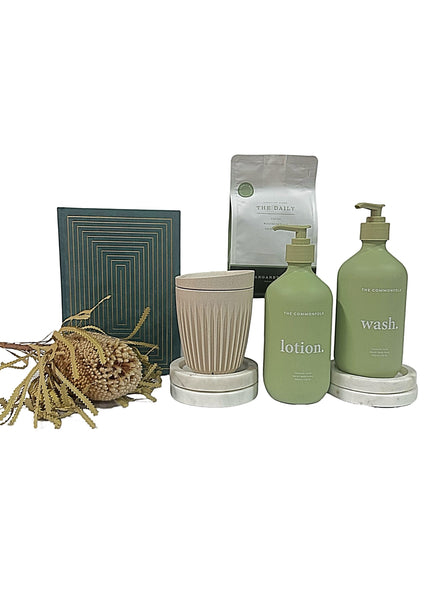 A gift set arrangement including a green bottle of lotion, a green bottle of body wash, a beige suede notebook, a brown huskee cup displayed on a white background.