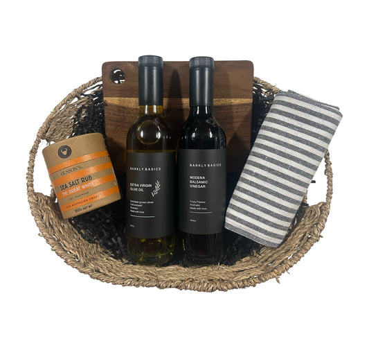 Wine bottles and a jar in a woven basket with a striped towel on a white background