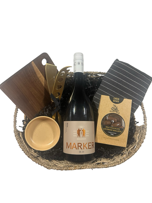 Wine gift basket with a bottle of Marker wine, a bowl, a board and knives on a white background.