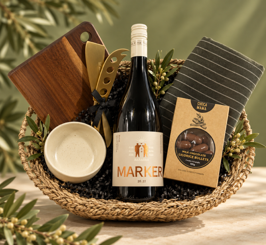 Wine gift basket with a bottle of Marker wine, a bowl, a board and knives on a green background.