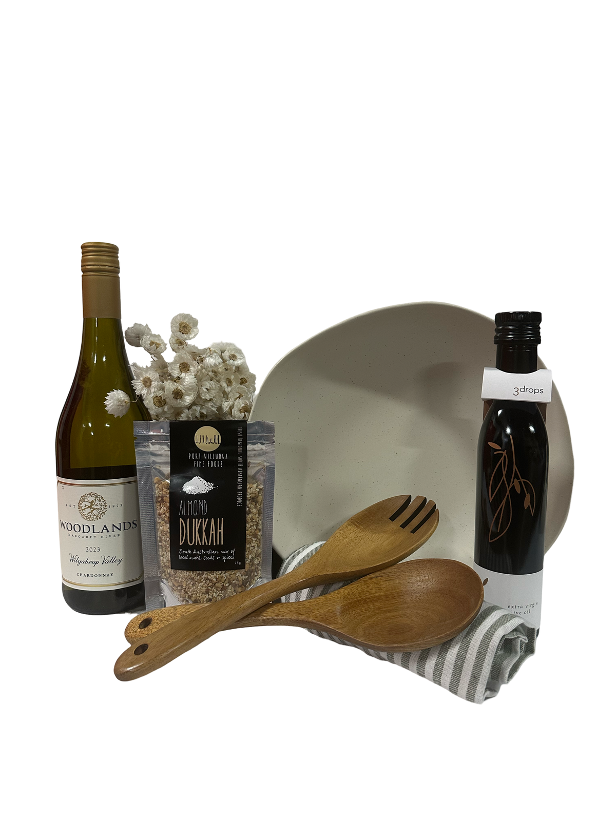 Bottle of wine, cream salad bowl, bottle of oil, packet of dukkah, wooden salad servers and striped tea towel