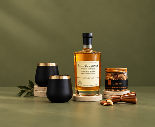 Limeburners single malt whisky bottle with black tumblers and a small container of nuts on a green background