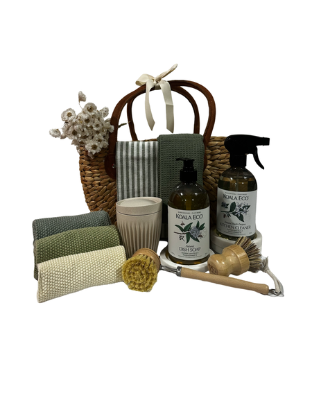 Woven basket with eco cleaning products, knit cloths, coffee cups, and wooden brushes.