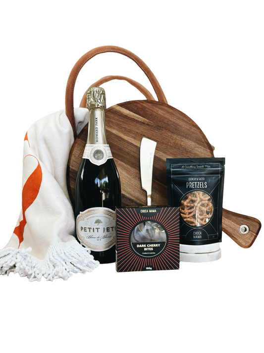 Gift basket with champagne, snacks, and a wooden board on a white background