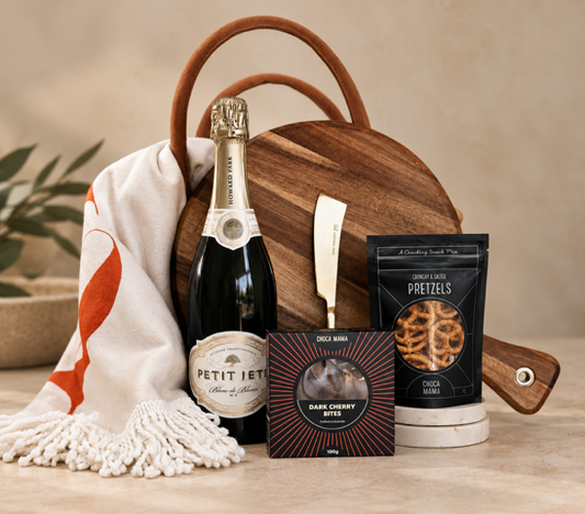 Gift basket with  picnic round tassel towel champagne, snacks, and a wooden board on a beige background