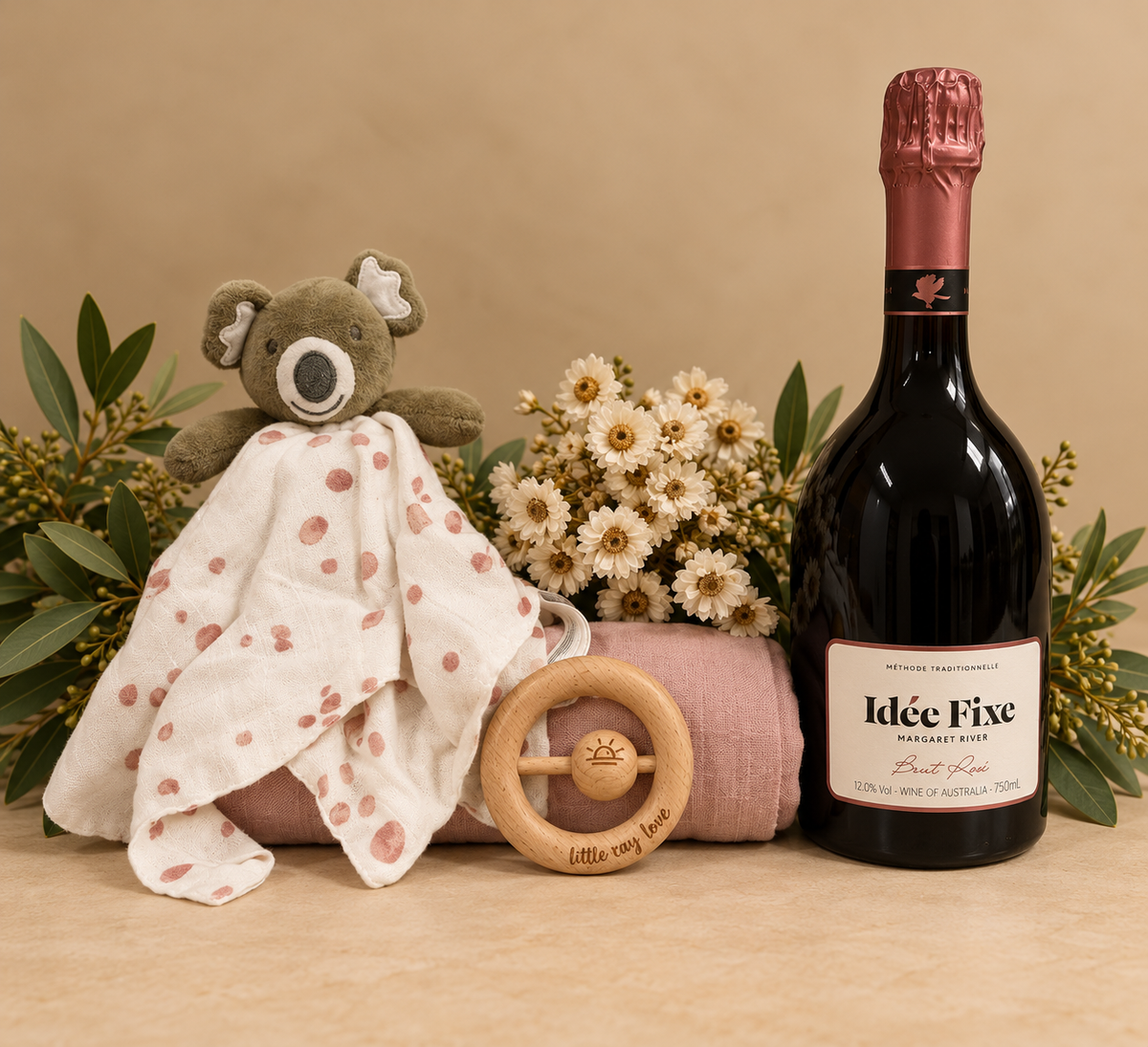 Gift box containing bottle of sparkling, baby comforter, swaddle and teether in blush tones.