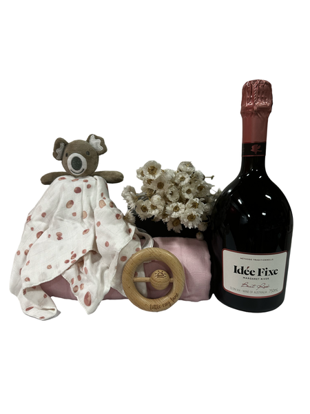 Gift box containing bottle of sparkling, baby comforter, swaddle and teether in blush tones.