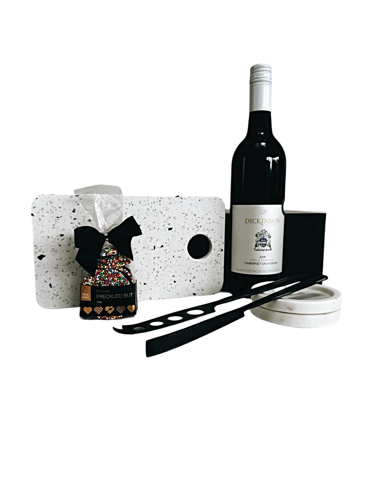 An assortment of wine and cheese accessories including a white terrazzo board, black cheese knives, a bottle of Cabernet Sauvignon, and gourmet chocolate Freckles, all presented in a magnetic gift box.